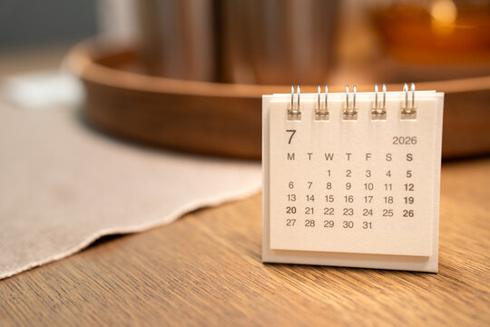 A small desk calendar of JULY 2026 on a wooden table with copy space. financial scheduling, commerce deadlines, and academic event management.