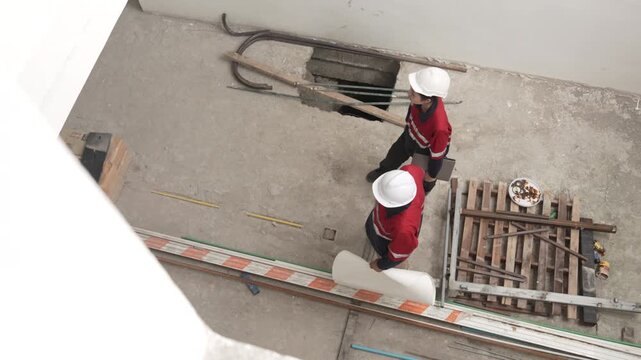Two construction workers wearing safety helmets discussing renovation progress and reviewing plans inside unfinished building interior.