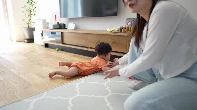 Soft light fills the cozy living room. Mother gently guides her baby on a patterned rug. The baby crawls toward her with curiosity. They share quiet, tender moments together