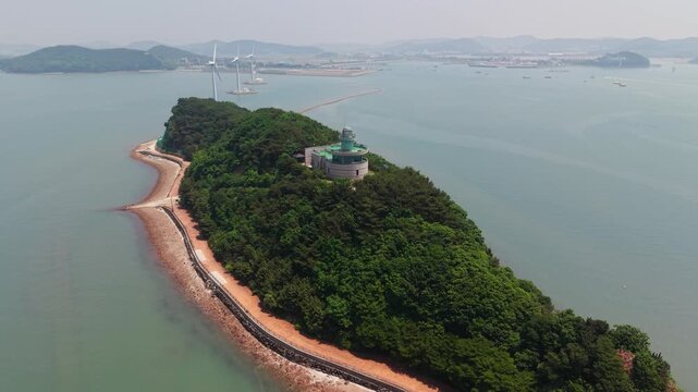Orbital aerial flight circles green hillside showcasing circular lighthouse tower overlooking vast ocean horizon at Nue Island