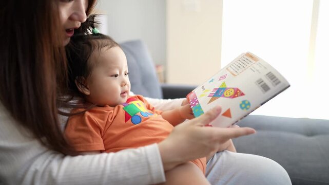 Mother reads to baby with gentle care. Child listens intently, eyes wide with wonder. Soft light fills cozy living room space. Perfect for parenting, education, or child development themes
