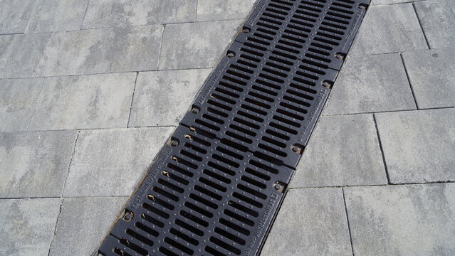 A metal drainage grate is installed on grey paving slabs in the city centre.