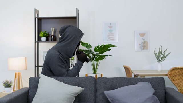 Masked Burglar Sneaking Behind Sofa in Living Room with Flashlight