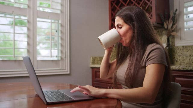 Woman sips coffee while scrolling on laptop
