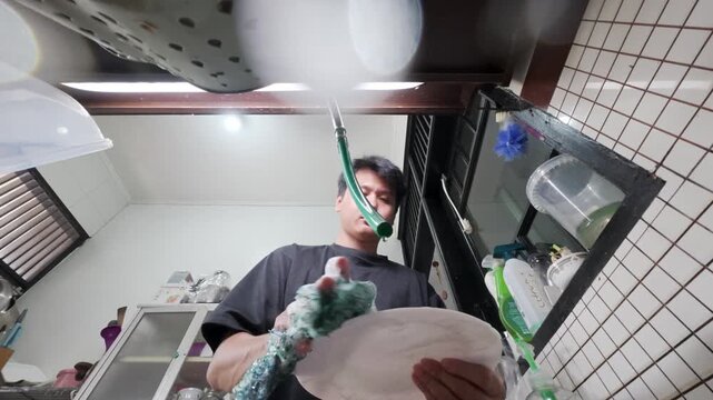 Man washing a soapy plate by hand in a kitchen sink, viewed from below