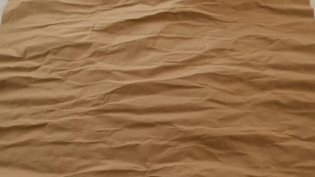 Static shot of brown kraft paper surface transitioning from smooth to crumpled with natural wrinkle texture