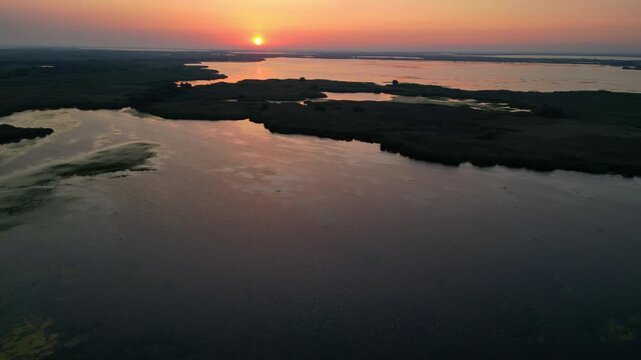 Spectacular high angle view of a golden sunrise over the Danube Delta UNESCO biosphere reserve. Scenic flyover above glowing water channels and wild reed vegetation in Romania.