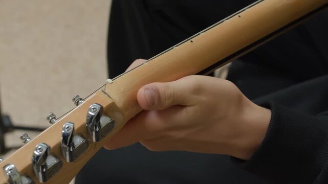 Child hand gripping wooden guitar neck showing metal tuning pegs, demonstrating proper instrument handling during music practice or lesson.