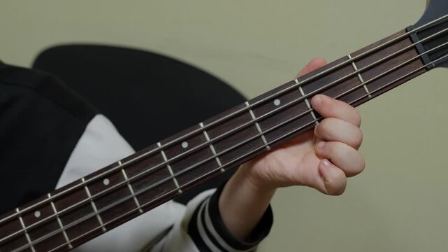 Close up of child hand fretting strings on dark acoustic guitar neck, learning to play music instrument against neutral background.
