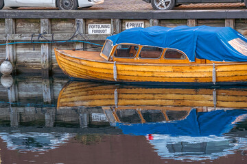 Obraz premium Traditional Danish Wooden Motorboat Moored by a Wooden Pier, Water Reflection Concept, Copenhagen