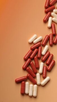 Red and white pills falling on table with tablets pharmaceutical industry concept on orange background