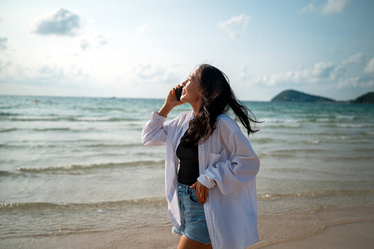 Cheerful woman talking on a smartphone during a sunny day at a tropical beach on summer vacation
