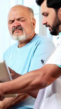 Indian Asian male doctor explaining a medical prescription or case report to a senior old-aged male patient in his OPD, ensuring clarity on treatment, dosage, and healthcare in a cozy clinic setting