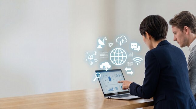 Two business colleagues analyzing global data charts on laptop, surrounded by holographic icons of cloud storage, satellite connection, wifi signal and world map, depicting