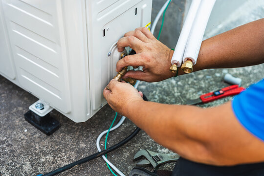 Technician connecting refrigerant lines to an outdoor air conditioner unit, Close-up of HVAC worker installing copper piping on an air conditioning condenser outdoors