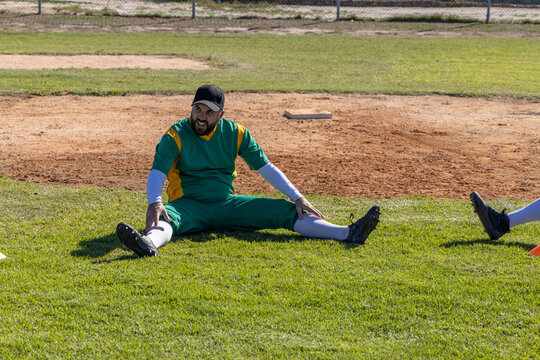 Vertical video: Stretching player warming up on grass at field, reaching foot to base, in uniform
