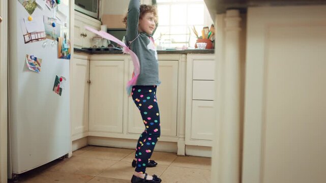 Wings, dancing or child with smile in kitchen, creative expression or costume for imagination growth. Playing, spoon and happy girl with fantasy dress up for development, home and moving to music