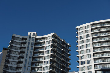 Naklejka premium Modern high rise apartment buildings rise against a clear blue sky, highlighting angular balconies, repeating geometric patterns, and a sleek urban living aesthetic.