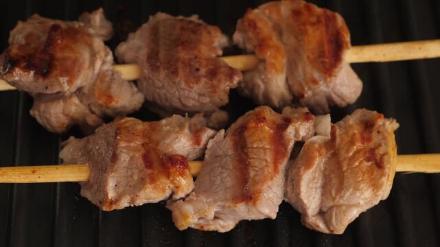 Juicy meat skewers on wooden sticks are grilled on an electric grill. The close-up shot demonstrates an appetizing crust with marks from the hot ribbed surface