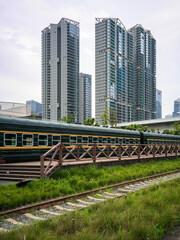 Fototapeta premium Vintage green train on grassy tracks contrasting with modern residential high-rise buildings
