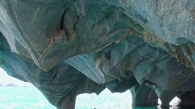 Witness the breathtaking beauty of the Marble Caves on General Carrera Lake. Intricate blue-gray formations meet vibrant azure waters during a bright daytime exploration in Patagonia.