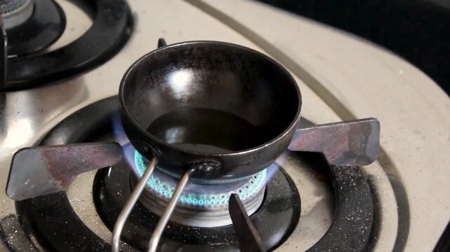 Small iron tadka pan heats oil over blue gas flame for traditional Indian tempering. Perfect for food documentaries, recipe videos, and South Asian cooking content.