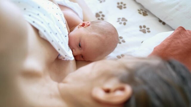 Intimate high angle view of a newborn baby breastfeeding, suckling on the mother's breast for nourishment. The scene highlights the maternal bond, love, and natural infant feeding process