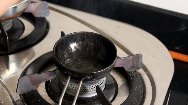 Black iron tadka pan with spice and chilli residue resting on gas burner after tempering. Perfect for Indian recipe transitions, food docs, and authentic cooking B-roll.