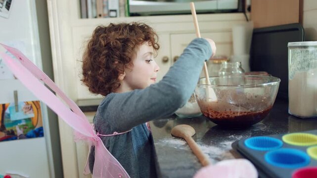 Girl, butterfly wings and baking in kitchen, development and learn culinary skills with ingredients. Child, growth and kid with creative costume, cooking and dessert preparation with recipe in house