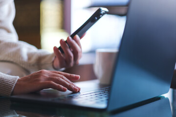 Fototapeta premium Closeup image of a woman using smart phone and laptop computer in cafe