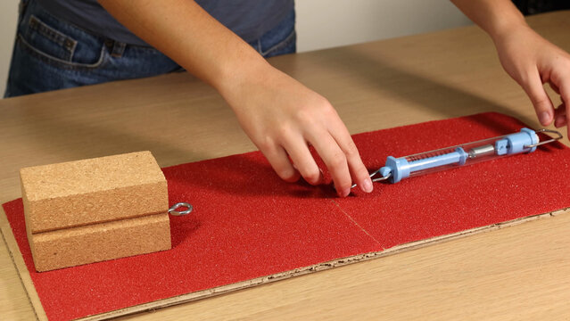 Hands Setting Up Physics Friction Experiment with Spring Scale and Block