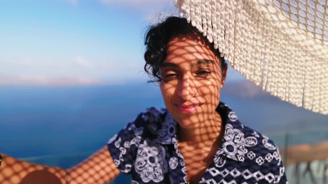 Beautiful young Indian woman with curly dark hair smiles warmly beneath a white woven macrame umbrella that casts intricate diamond-shaped shadow patterns across her face during golden hour sunset.