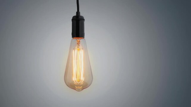 Vintage glowing Edison light bulb hanging with warm filament on gray background
