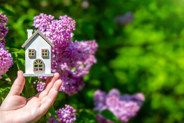 Naklejka premium The girl holds in her hand the symbol of the house against the background of blooming lilac 