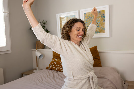Mature woman stretching arms in bathrobe after waking up