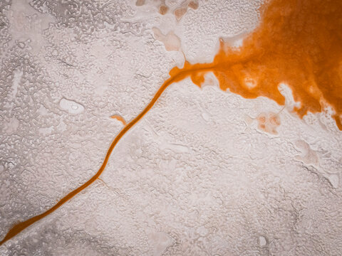 An orange river cuts through a cracked salt flat