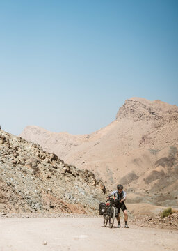 Cyclist struggles pushing bike up desert road in Oman