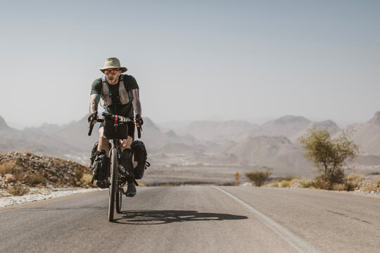 Man bikepacking on a hot desert highway in Hajar Mountains, Oman