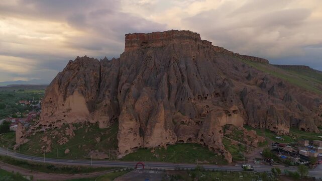 sunset drone aerial of Selime Cathedral monastery structures built into a steep mountain ridge. Dramatic geological terrain and landmark historical architecture in Turkey