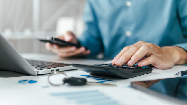 A male accountant calculating annual car tax, income and expense calculations, and analyzing trading reports; concepts of annual vehicle tax, and financial and tax systems.