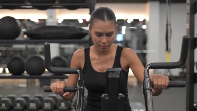 Determined Isan Thai Woman Training on stationary Air Bike at Night in Gym