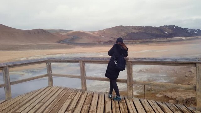 Female on a wooden platform, gazing out at the expansive geothermal region of Hverir in Iceland, featuring its otherworldly Martian esque scenery