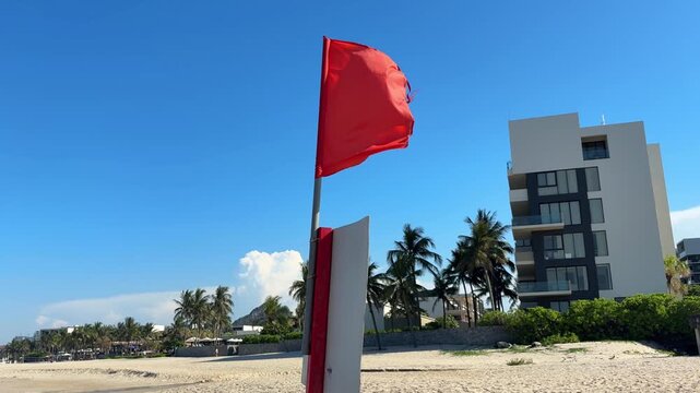 Video of a red warning flag on a beach by the sea, indicating dangerous swimming conditions and restricted access to water. Coastal safety concept with ocean waves and seaside atmosphere.