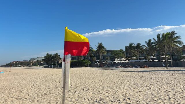 Video of a red warning flag on a beach by the sea, indicating dangerous swimming conditions and restricted access to water. Coastal safety concept with ocean waves and seaside atmosphere.