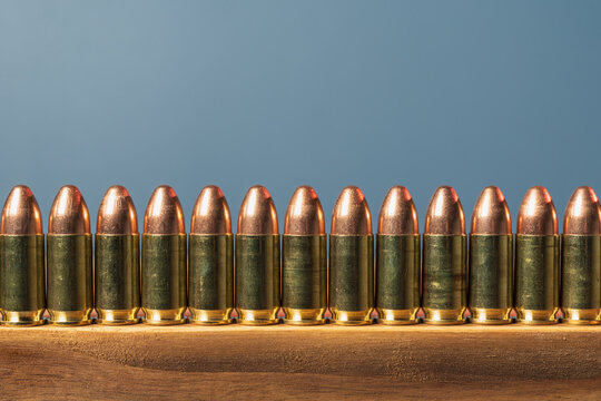Row of 9mm pistol ammunition bullets lined up on a wooden surface with a blue background and a large copy space above