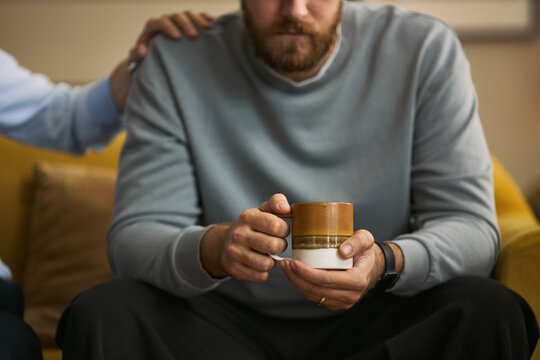 Caucasian young adult men sitting together, offering shoulder support and holding mug, expressing male friendship and emotional care. Useful for mental health, support group, trust campaigns