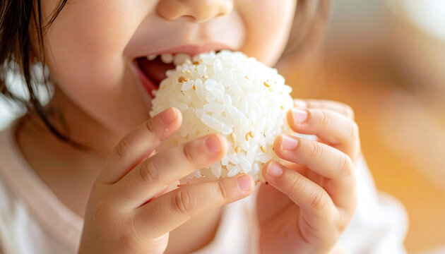 おにぎりを両手でしっかり持ち頬張る日本人の幼い子供のクローズアップ