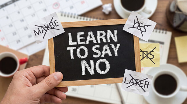 Hand holding a learn to say no chalkboard on a desk, rejecting commitments like yes, maybe, and later