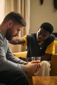 Vertical shot of young adult Black man comforting Caucasian male friend, offering emotional support during difficult conversation. Useful for mental health, friendship, counseling campaigns