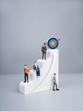 Miniature business people climbing steps toward target achievement and career growth success. Concept of leadership, professional development, motivation, business strategy and goal accomplishment.